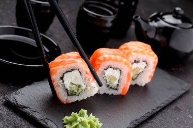 Somon suşi rulo taş tabağa çubuklarla beton arka plan üzerinde.