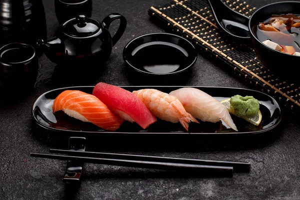 Sushi auf einem schwarzen Teller und Misosuppe vor dunklem Betonhintergrund — Stockfoto