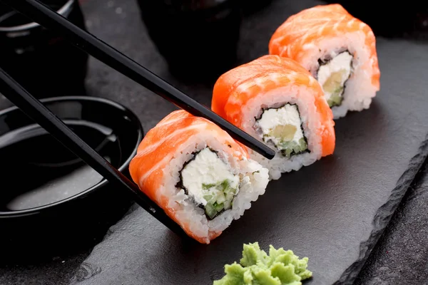 Rolo de sushi de salmão em uma placa de pedra com pauzinhos sobre fundo de concreto . — Fotografia de Stock