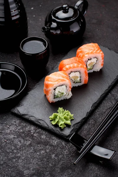 Salmon sushi roll on a stone plate with chopsticks over concrete background. — Stock Photo, Image