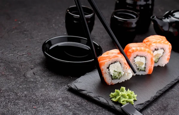 Salmon sushi roll on a stone plate with chopsticks over concrete background. — Stock Photo, Image