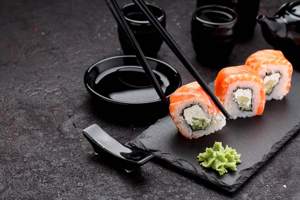 Salmon sushi roll on a stone plate with chopsticks over concrete background. — Stock Photo, Image