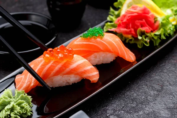Japanilaista ruokaa. Lohi sushi nigiri mustalla lautasella syömäpuikoilla . — kuvapankkivalokuva