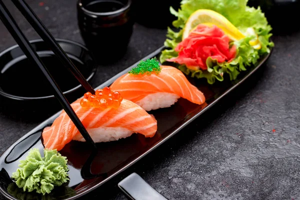 日本の料理。箸で黒い皿にサーモン寿司にぎり. — ストック写真