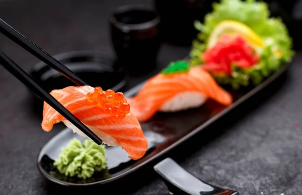 Japanese cuisine. Salmon sushi nigiri on a black plate with chopsticks. — Stock Photo, Image