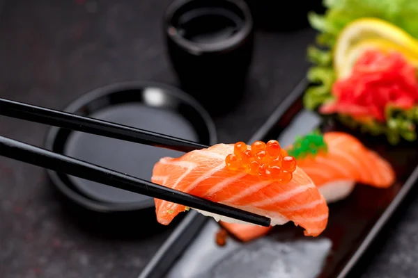 Japon mutfağı. Somon suşi nigiri yemek çubukları ile siyah bir plaka üzerinde. — Stok fotoğraf