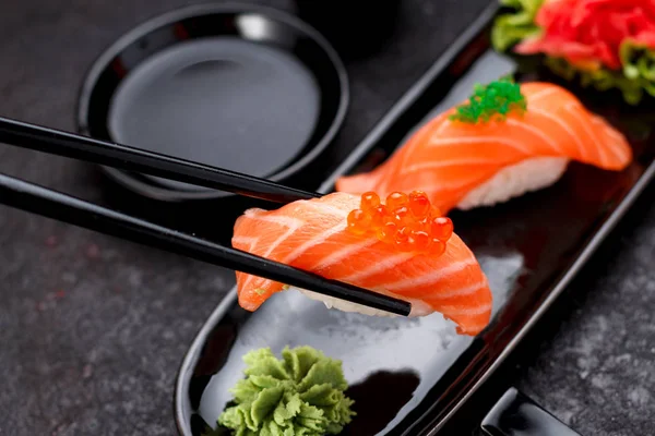 Japanse keuken. Zalmsushi nigiri op een zwarte plaat met stokjes. — Stockfoto