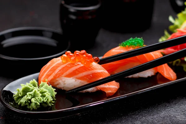 Cuisine japonaise. Saumon sushi nigiri sur une assiette noire avec des baguettes . — Photo