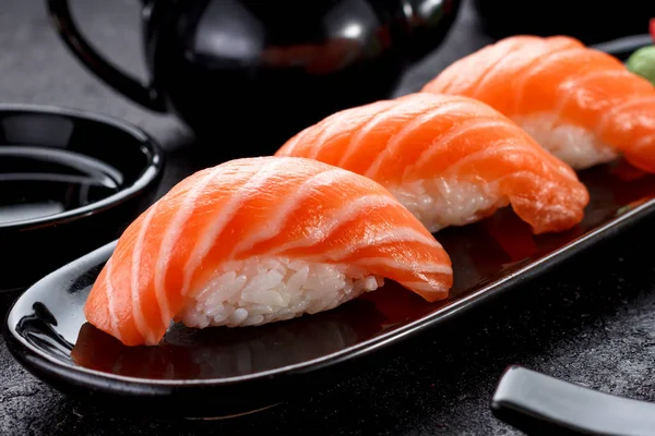 Sushi di salmone con salsa di soia su un piatto nero e sfondo di cemento scuro . — Foto Stock