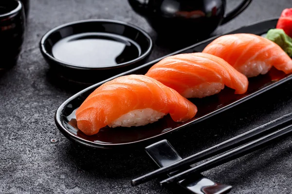 Zalmsushi met sojasaus op een zwarte plaat en de donkere betonnen achtergrond. — Stockfoto