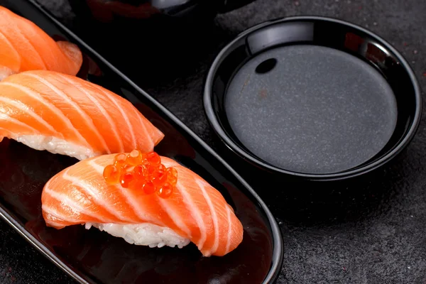 Sushi au saumon avec sauce soja sur une assiette noire et fond béton foncé . — Photo