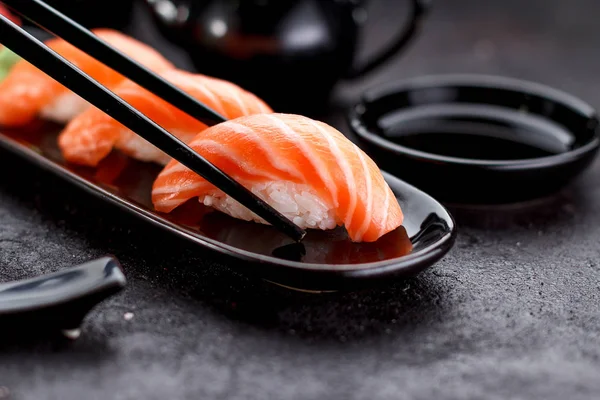 Salmon sushi with soy sauce on a black plate and dark concrete background. — Stock Photo, Image