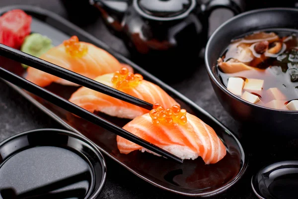 Japanse keuken. Zalmsushi nigiri en miso soep op zwarte plaat een donkere tafel. — Stockfoto