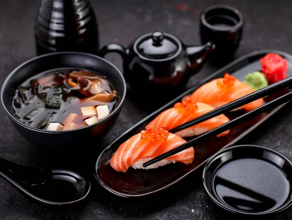 Japanska köket. Lax sushi nigiri och miso soppa på svarta plåten ett mörkt bord. — Stockfoto