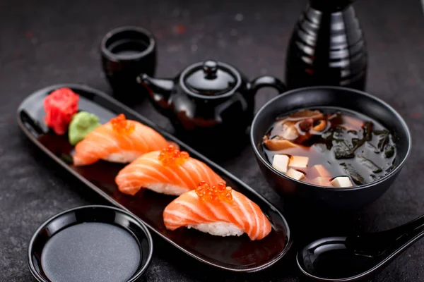 Japanese cuisine. Salmon sushi nigiri and miso soup on black plate a dark table. — Stock Photo, Image