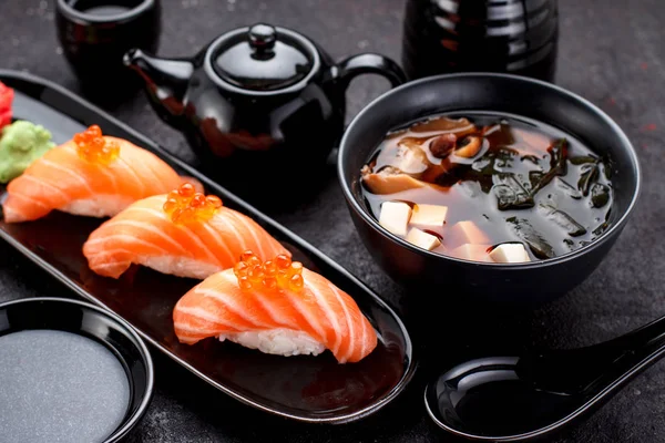 Japanese cuisine. Salmon sushi nigiri and miso soup on black plate a dark table. — Stock Photo, Image