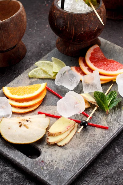 Coconut with ice and fresh fruits (grapefruit, kiwi, orange ) and mint over concrete background. — Stock Photo, Image