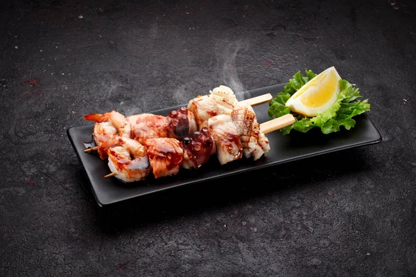 Tasty seafood skewers and soy sauce over dark concrete background — Stock Photo, Image