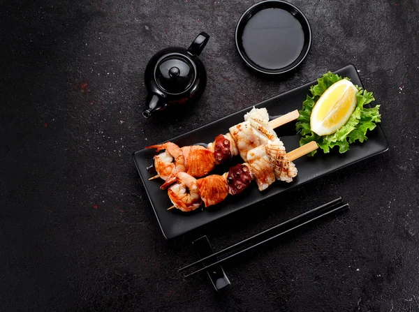 Tasty seafood skewers and soy sauce over dark concrete background — Stock Photo, Image