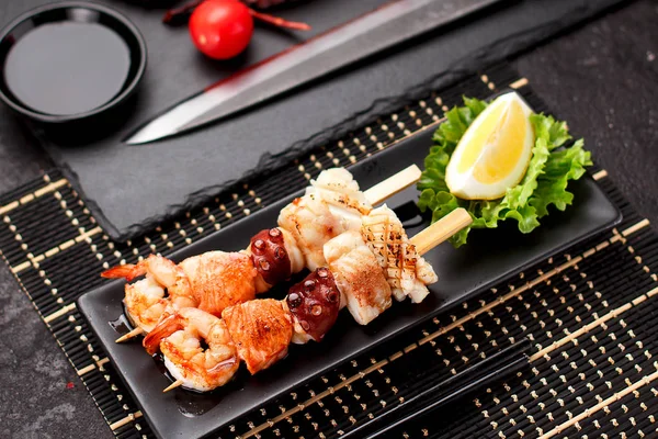 Tasty seafood skewers and soy sauce over dark concrete background — Stock Photo, Image