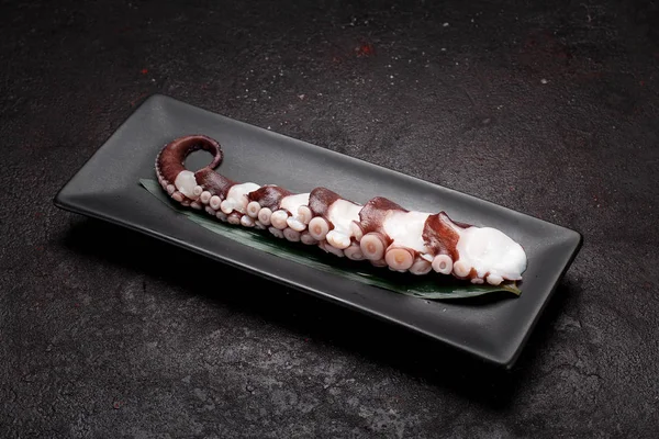 The tentacles of the octopus on a black plate and dark concrete background — Stock Photo, Image
