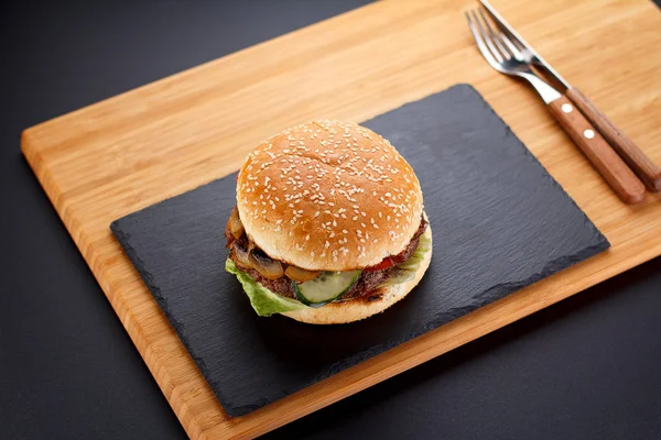 Big burger on a stone plate and wooden background.