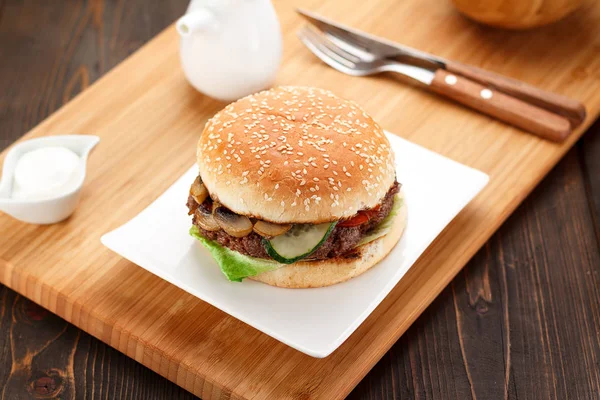 Big burger on a white plate, wooden board and background.