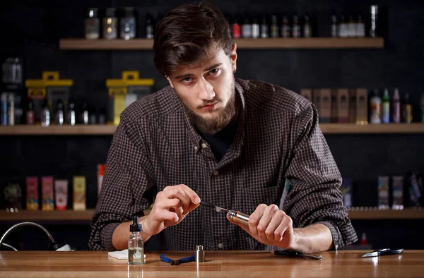 Vape. En man i en vape bar (butik) reparerar e-cigarett. Stockbild