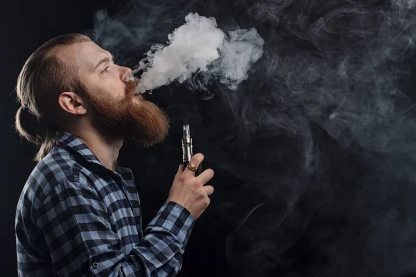 Vaping man innehar en mod. Ett moln av ånga. Svart bakgrund. Studio fotografering. — Stockfoto