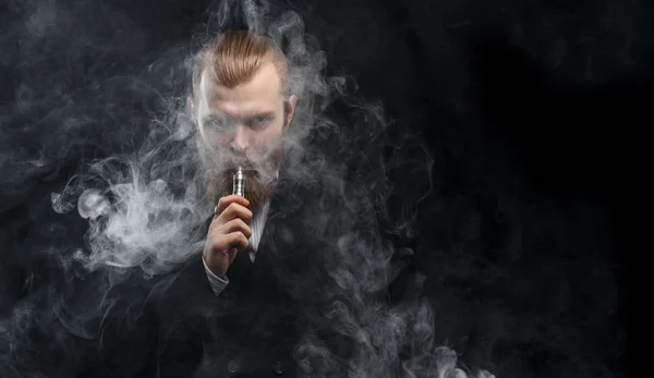 Vaping man holding a mod. A cloud of vapor. Black background. Studio shooting.