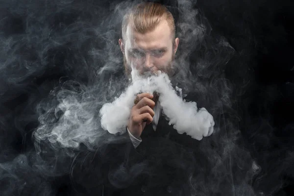 Vaping man innehar en mod. Ett moln av ånga. Svart bakgrund. Studio fotografering. — Stockfoto