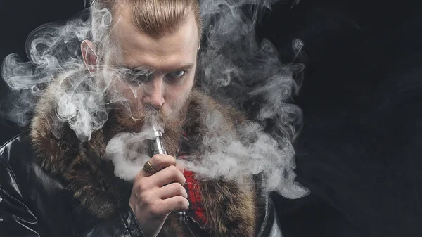 Vaping man holding a mod. A cloud of vapor. Black background. Studio shooting. — Stock Photo, Image
