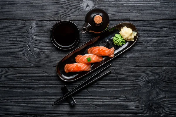 Japanese cuisine. Salmon sushi nigiri with soy sauce on a dark wooden background.
