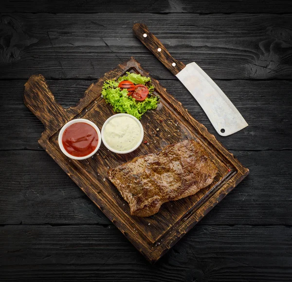 Gegrilde biefstuk met sauzen op een bord. Donkere houten tafel. — Stockfoto