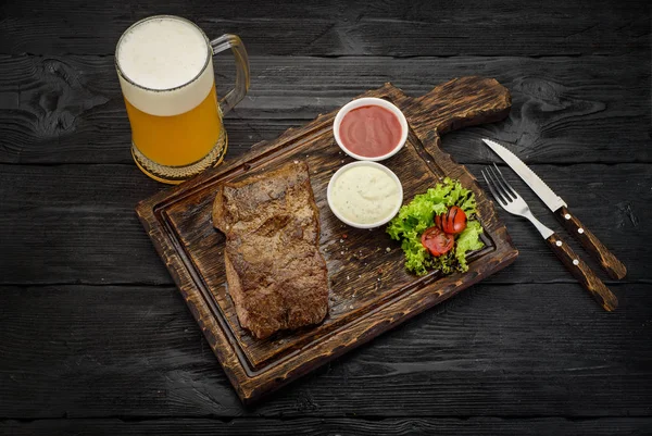 Grilovaný hovězí steak s omáčkami na desce. Tmavý dřevěný stůl. — Stock fotografie