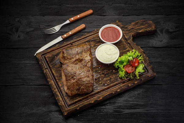 Gegrilde biefstuk met sauzen op een bord. Donkere houten tafel. — Stockfoto