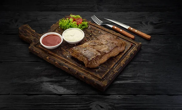 Grillezett marhahús steak szószok egy táblán. Sötét fából készült asztal. — Stock Fotó