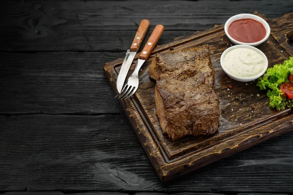 Gegrilde biefstuk met sauzen op een bord. Donkere houten tafel. — Stockfoto