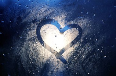 Kalp pencereye. Yağmurda sisli camlara parmak ile boyanmış. Sokak lambasından parlak bir bokeh.