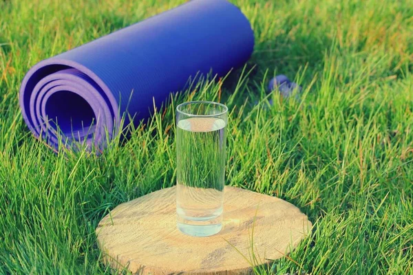 A glass of water on and a purple rubber sports mat on green grass for sports.
