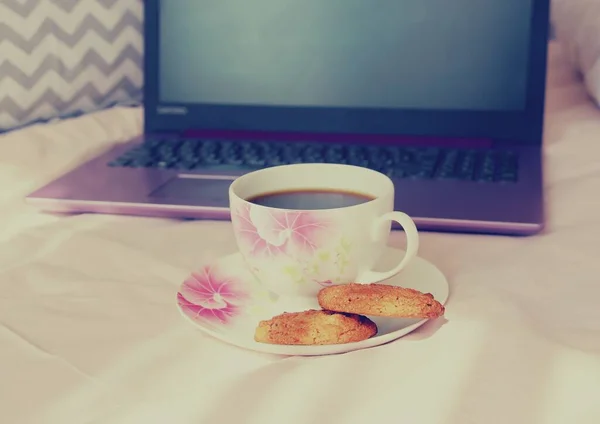 ピンクのベッドに紫色のノートパソコンでクッキーとお茶のカップ 自宅でのリモートワーク — ストック写真