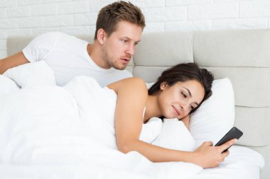 Genç çift, yakışıklı koca ve güzel karısı sabah erken saatlerde yatakta akıllı telefonlarını kontrol ederek uyandılar.