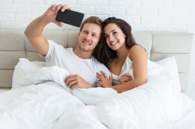 Genç çift, yakışıklı koca ve güzel karısı sabahın erken saatlerinde yatakta akıllı telefondan selfie çekerek uyandılar.