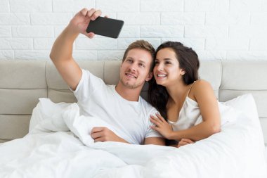 Genç ve mutlu bir çift yakışıklı koca ve güzel karısı sabahın erken saatlerinde yatakta akıllı telefondan selfie çekerek uyandılar.