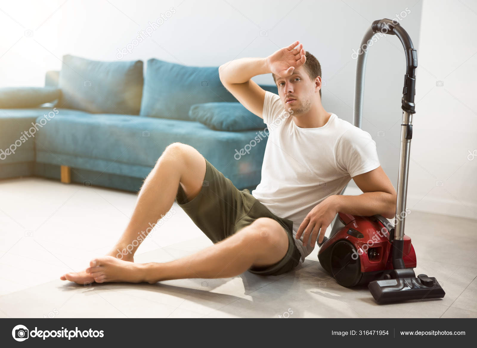 Handsome young fatigued man sitting near vacuum cleaner in the ...