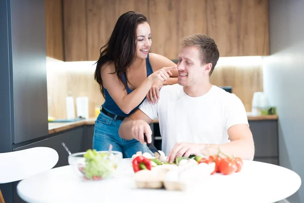 Jong paar koken ontbijt in de keuken samen vrouw knuffelen haar geliefde man en aanraken van zijn neus grappen familie tradities — Stockfoto