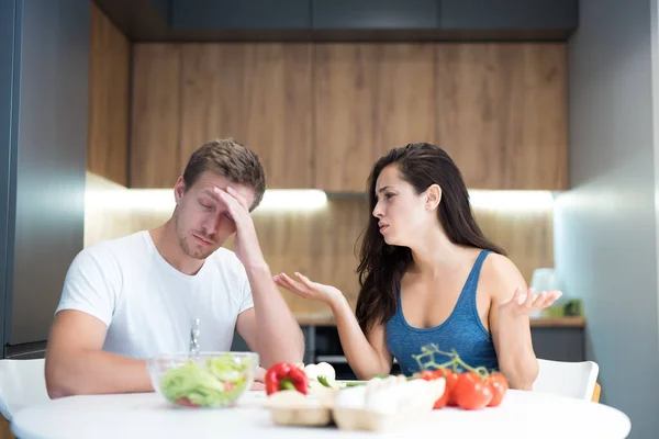 Young couple having fight while cooking breakfast in the kitchen husband looks tired and wife is irritated family quarrel — Stock Photo, Image