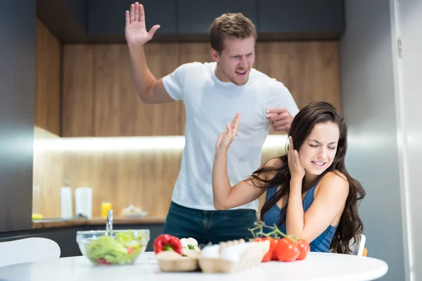 young couple having fight while cooking breakfast in the kitchen husband lifts his arm against his wife while she turns away family vilonce