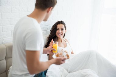 Genç adam lezzetli bir Fransız kahvaltısı hazırladı - ay çöreği ve portakal suyu sevgili karısı için yatakta mutlu bir sabah ailesi gibi görünüyor.