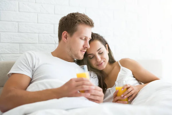 Счастливая молодая пара красивый мужчина и красивая женщина только что проснулся в яркой спальне утром пить апельсиновый сок идиллии семьи — стоковое фото